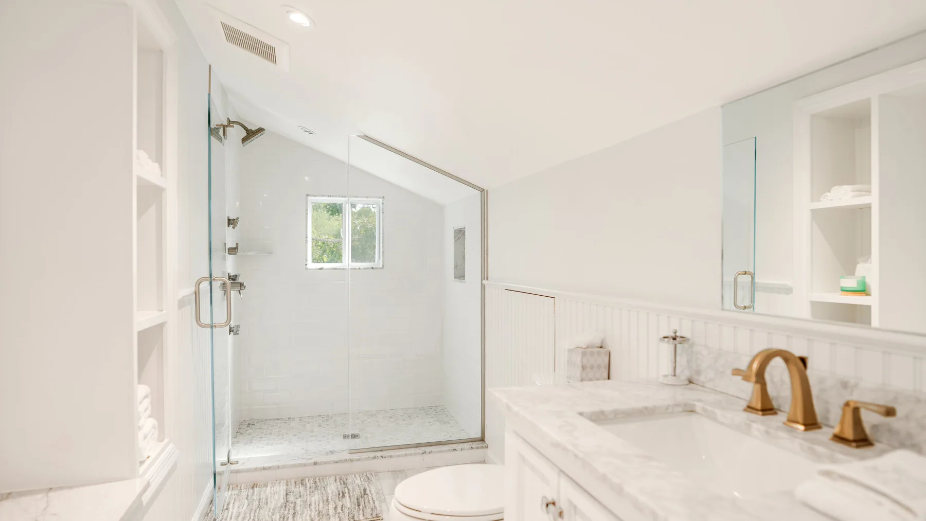 A bright bathroom with a glass shower and a long white vanity.