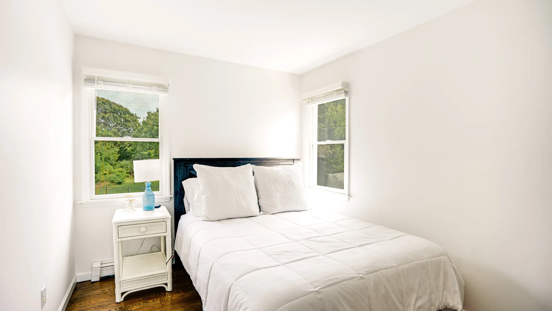 A bright bedroom with a bed between two windows.