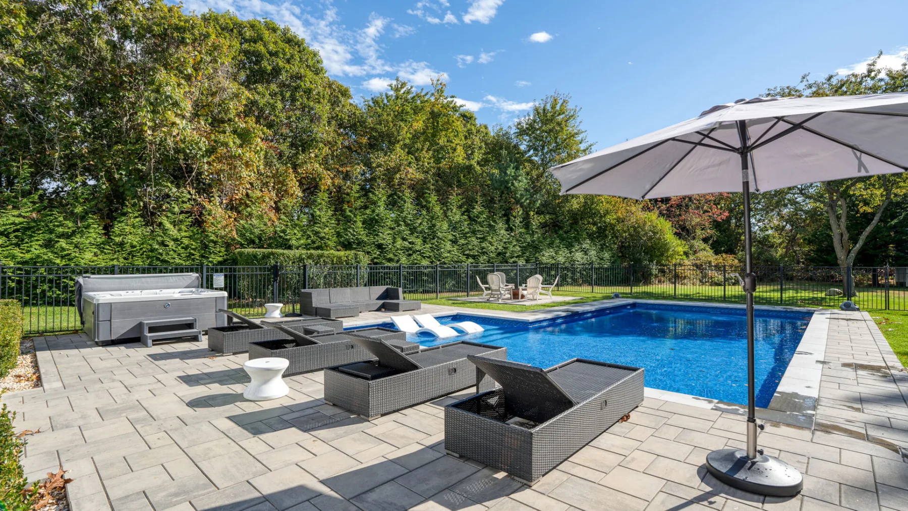 An outdoor pool and patio with lounge seating and a large umbrella.