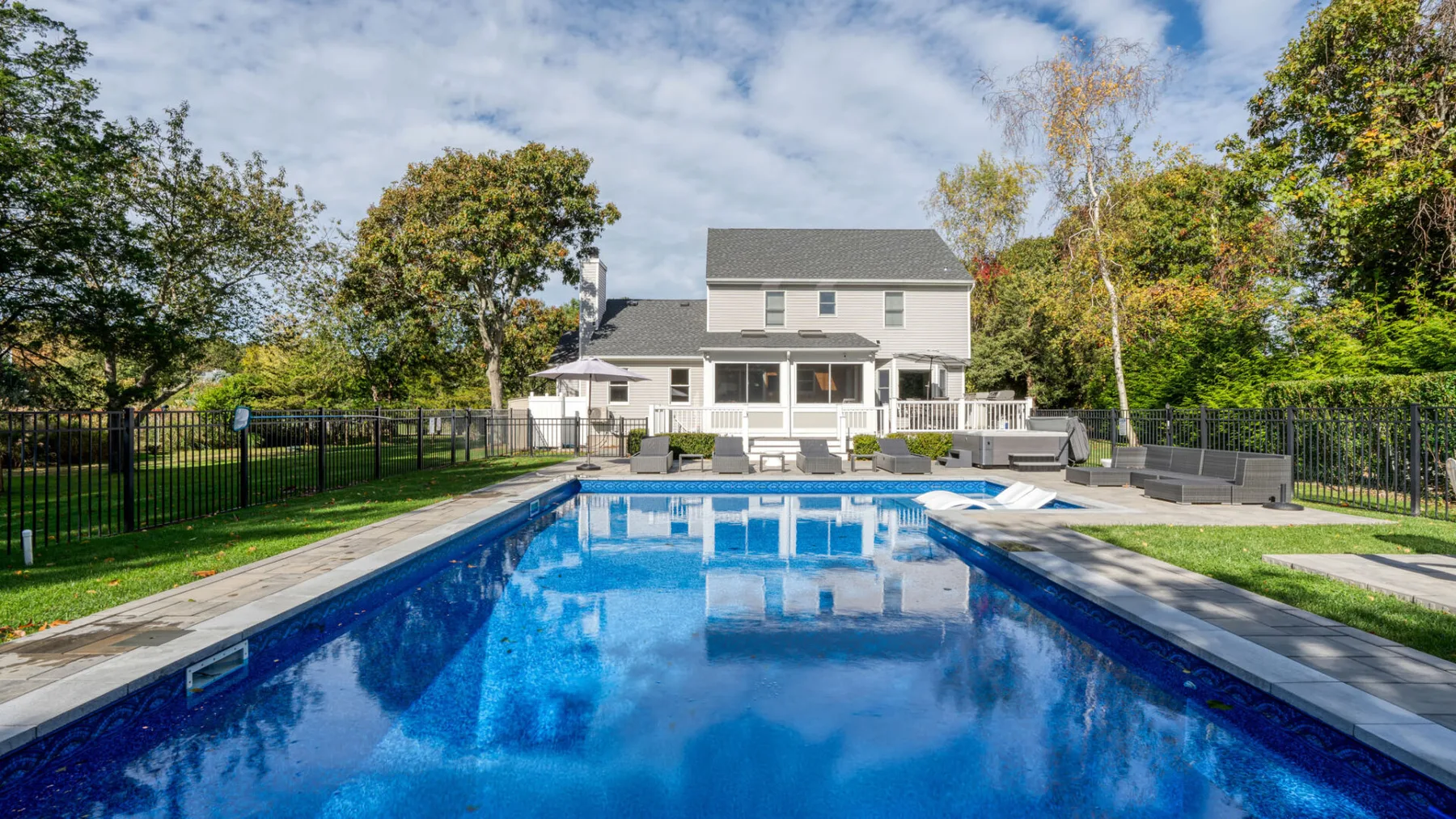 A backyard swimming pool stretches toward a large house surrounded by trees.