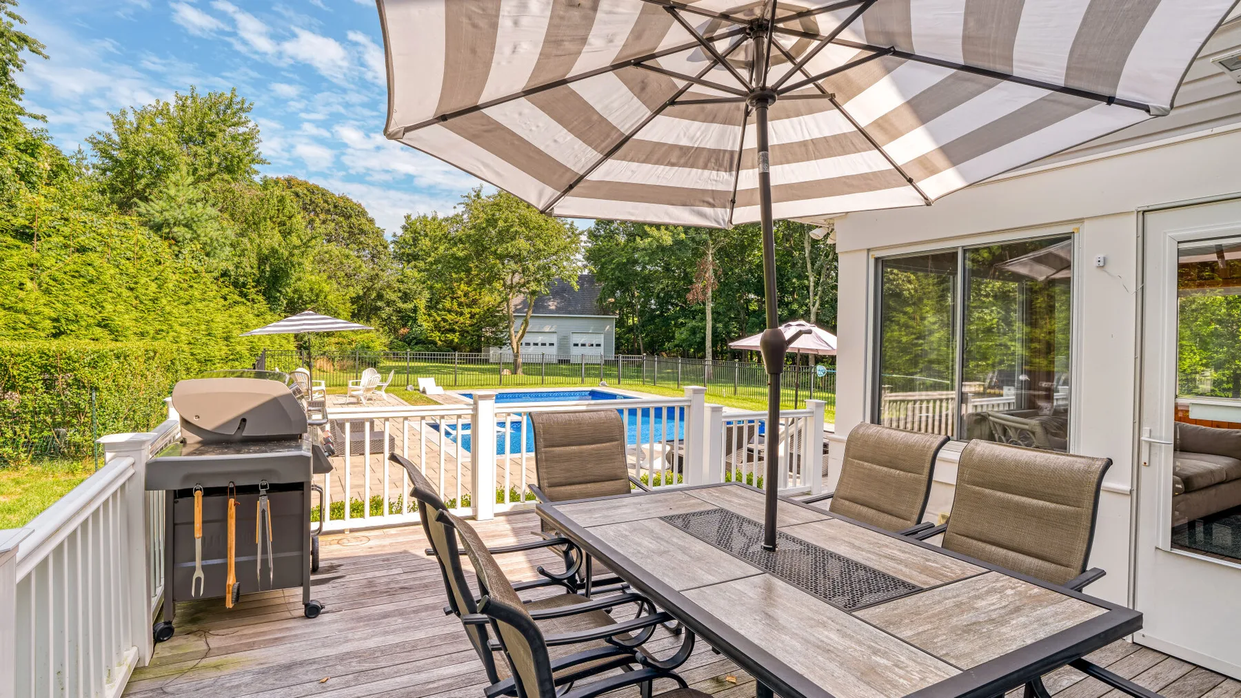 A patio dining area overlooks a swimming pool and green yard.