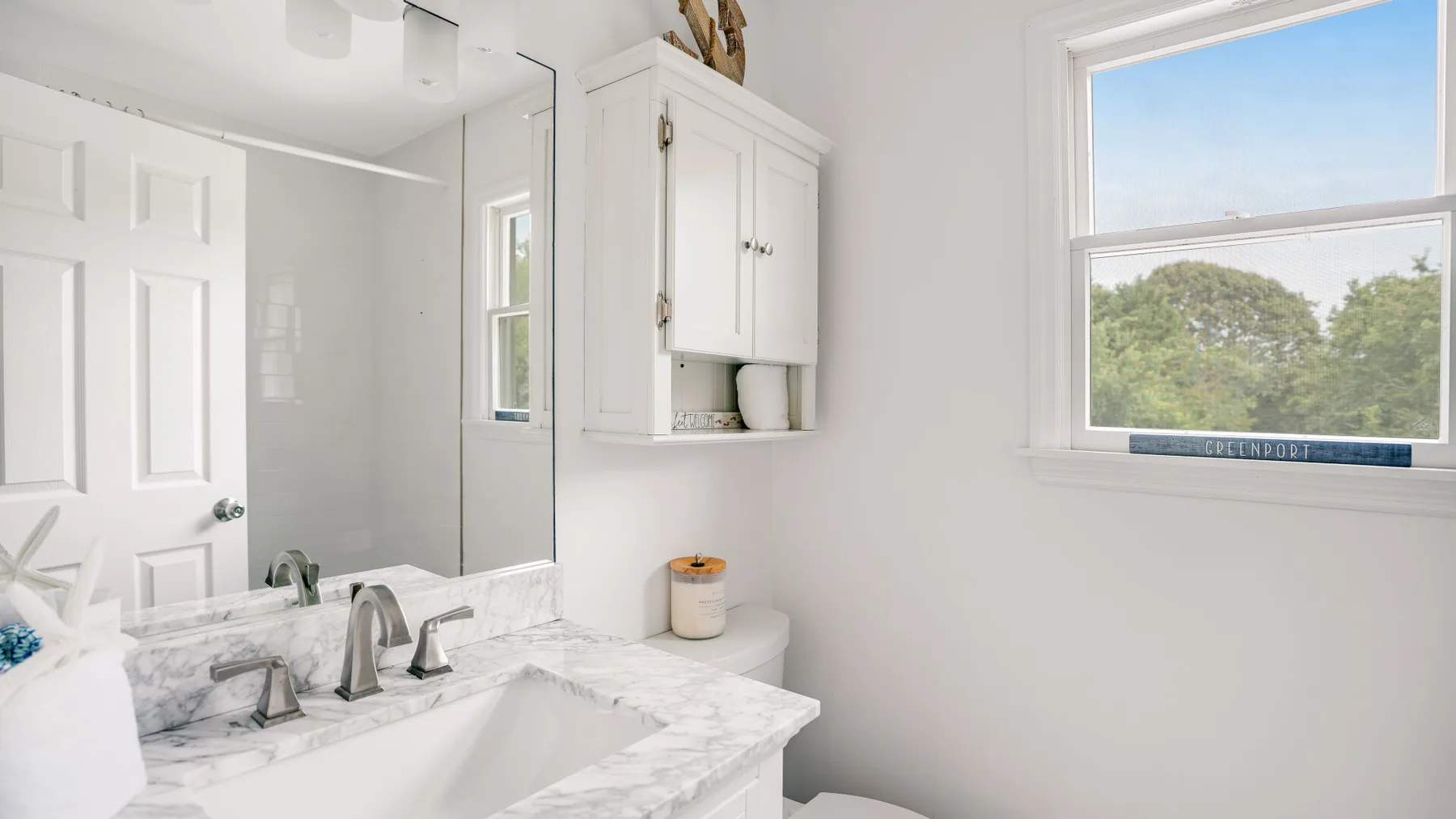 A bright bathroom with a marble-look vanity and a window overlooking trees.