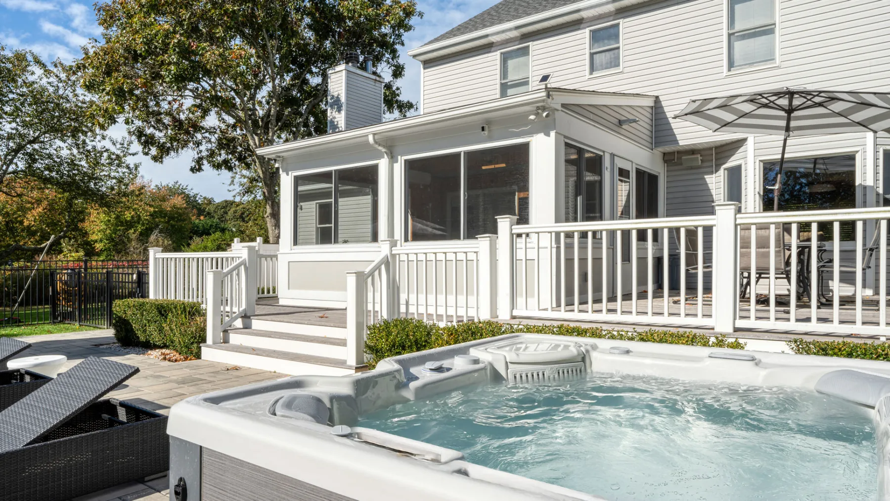 A backyard patio with a hot tub beside a white house and deck.
