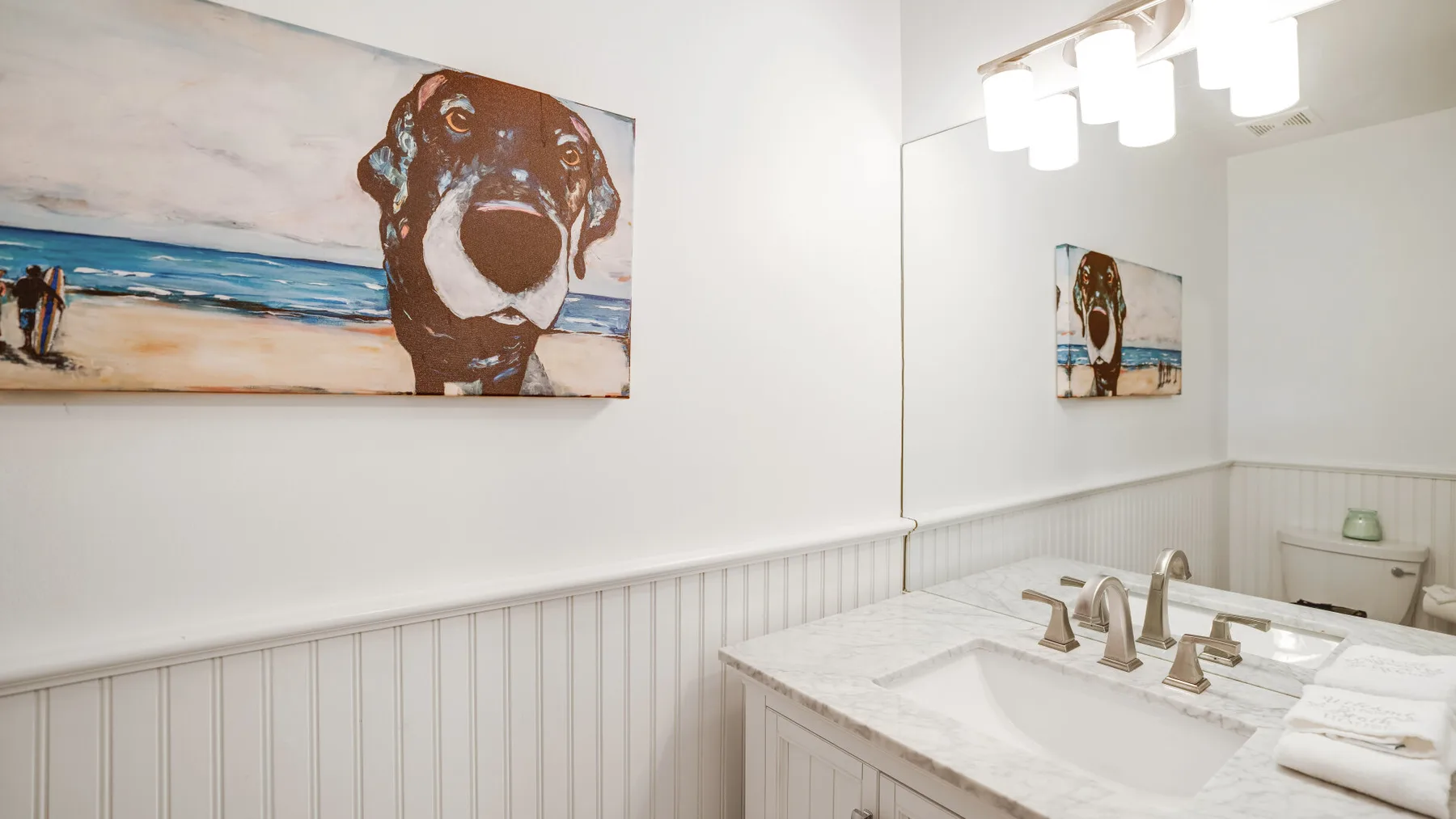 A bright bathroom with a wide vanity, mirror, and colorful dog artwork.