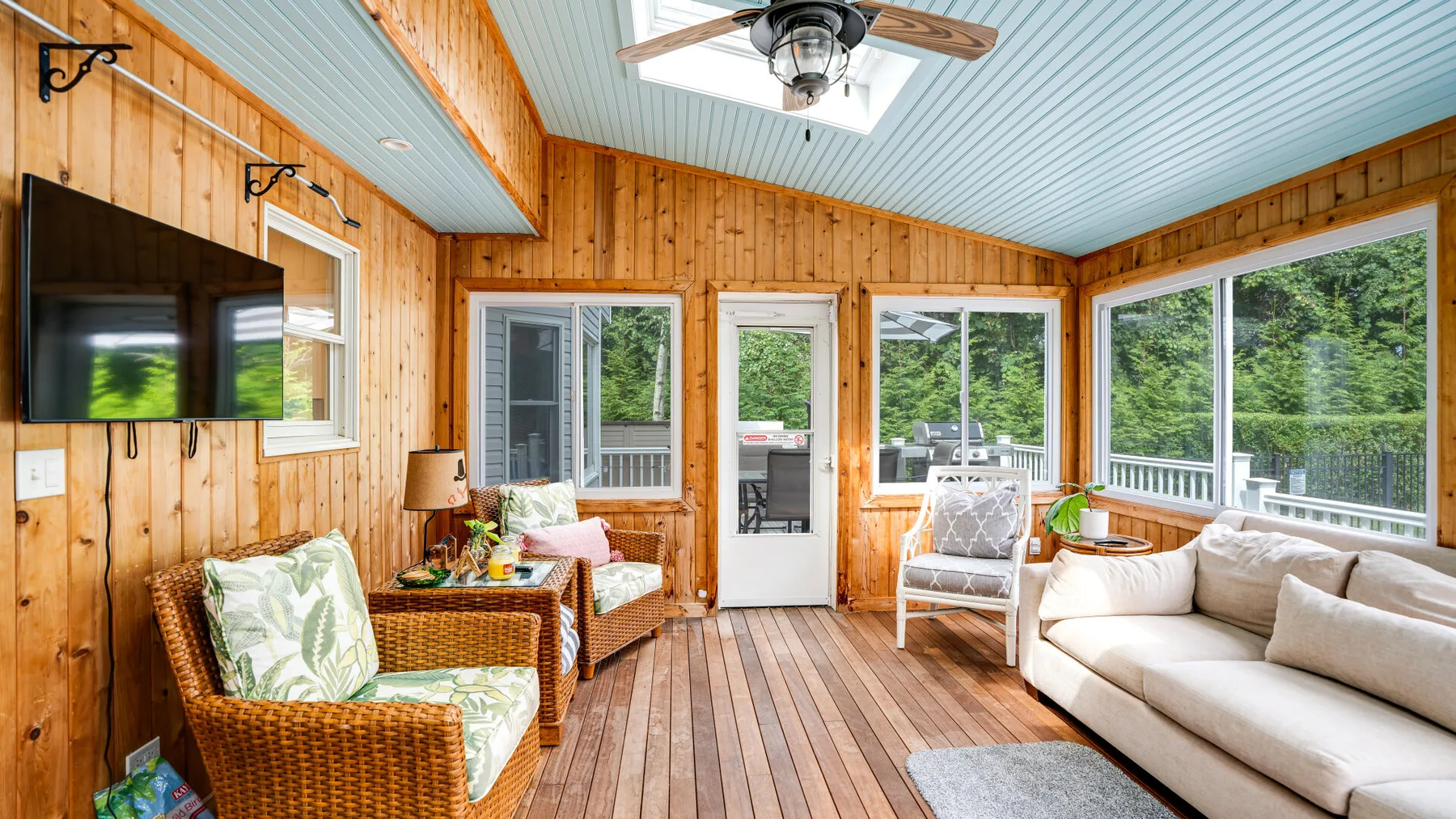 A wood-paneled sunroom with seating and large windows overlooking greenery.