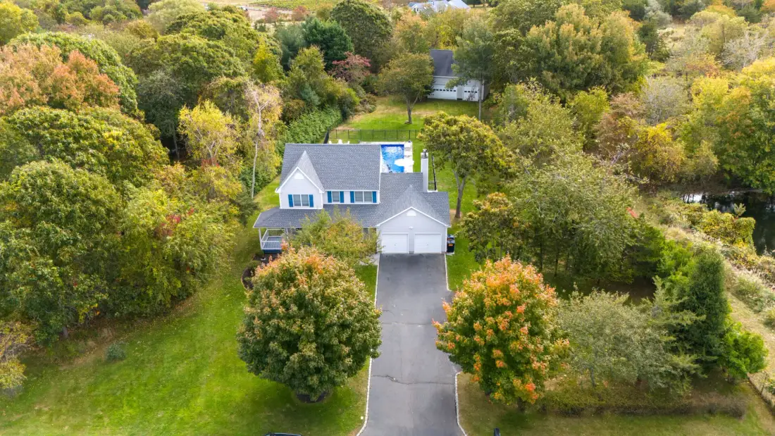 Aerial view of a house surrounded by trees, with a driveway and swimming pool.