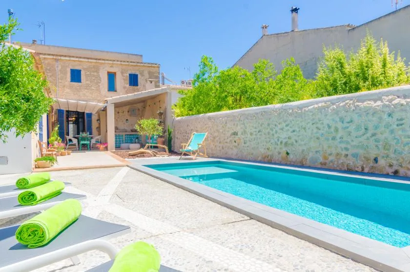 A sunny outdoor pool beside a stone courtyard and shaded seating.