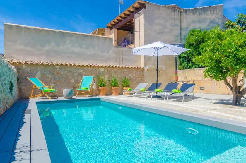 An outdoor swimming pool with lounge seating, an umbrella, and potted plants.