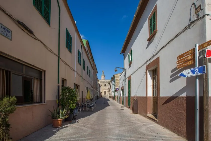 A narrow paved street runs between white buildings beneath a clear blue sky.