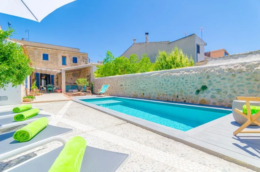 An outdoor swimming pool beside a sunlit patio with lounge seating.