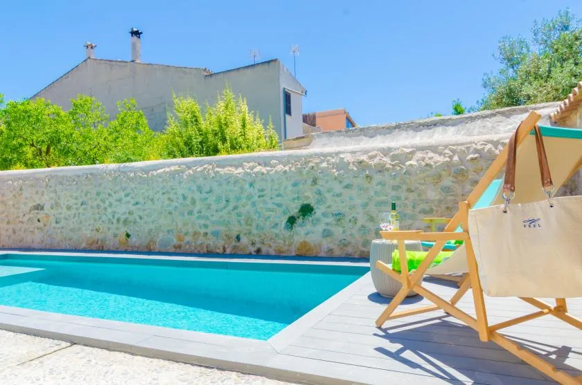 An outdoor swimming pool beside a pale stone wall and wooden deck chairs.