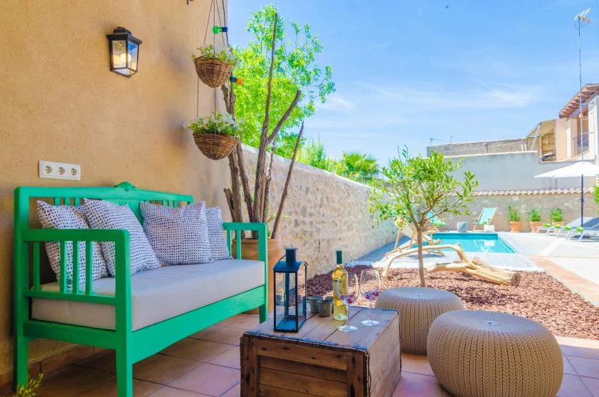 An outdoor patio seating area overlooks a swimming pool, with plants and a low table.