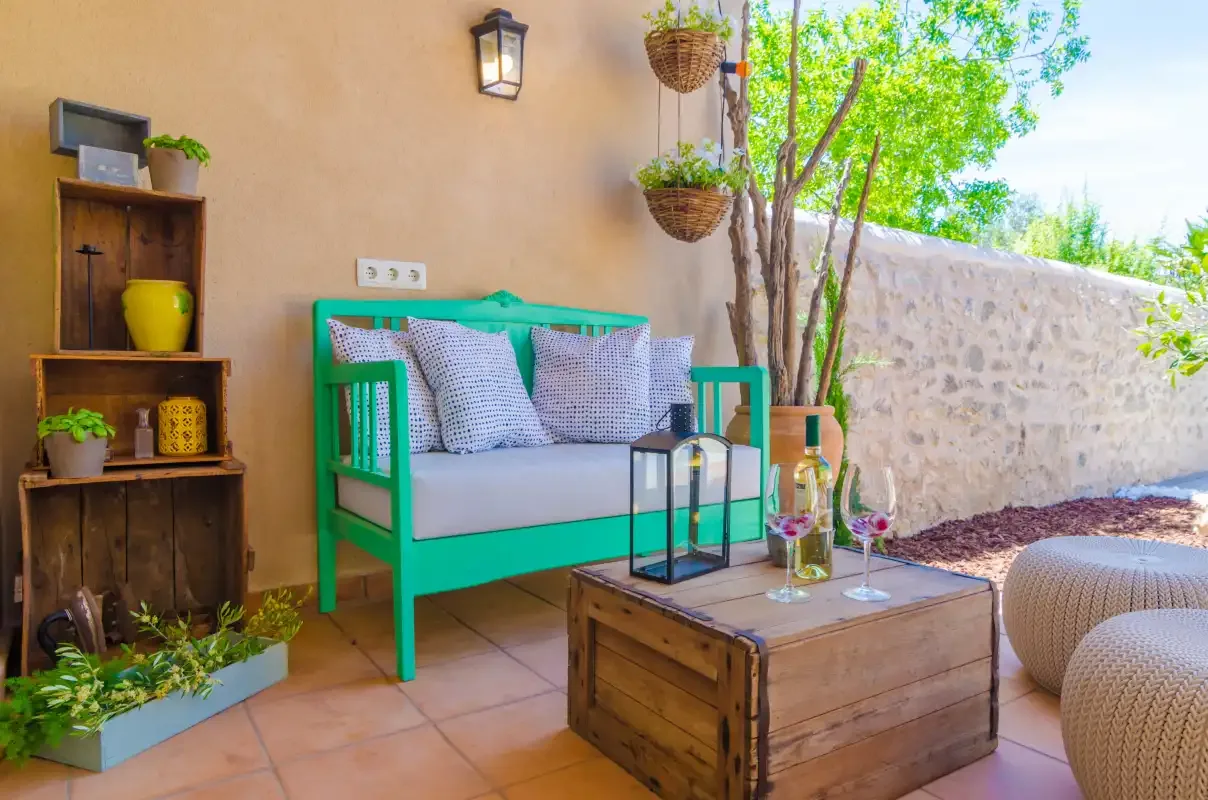 An outdoor seating area with a wooden table beside a stone wall and leafy tree.