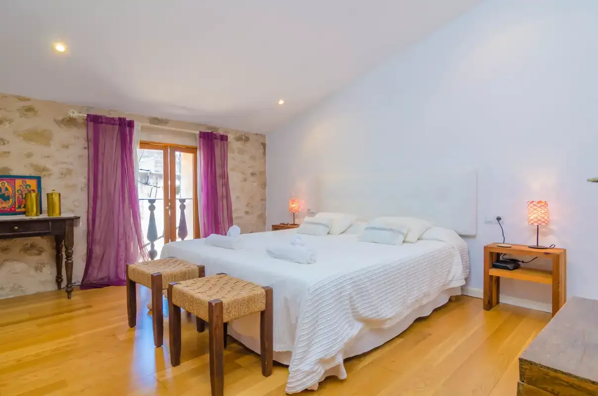A bedroom with a large bed, bedside tables, and a window with purple curtains.