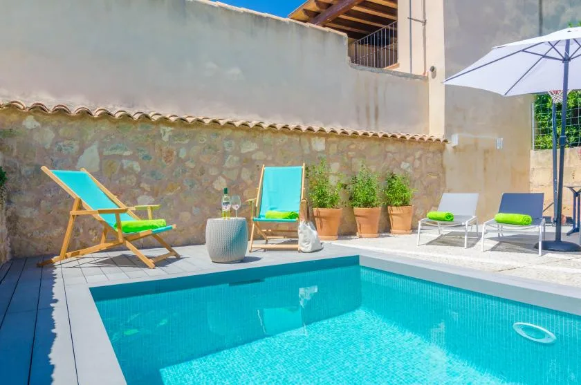 An outdoor swimming pool with lounge chairs and potted plants beside a stone wall.