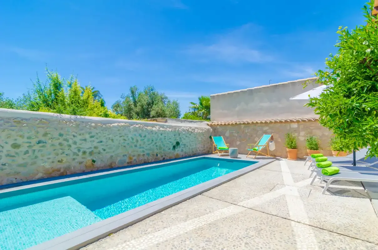 An outdoor swimming pool bordered by a stone wall and lounge seating.