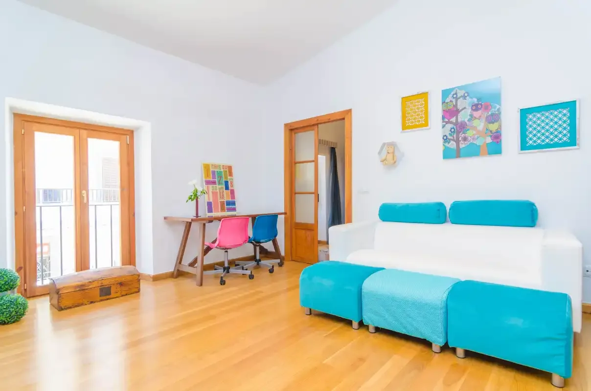 A bright living room with turquoise seating, a desk, and framed wall art.