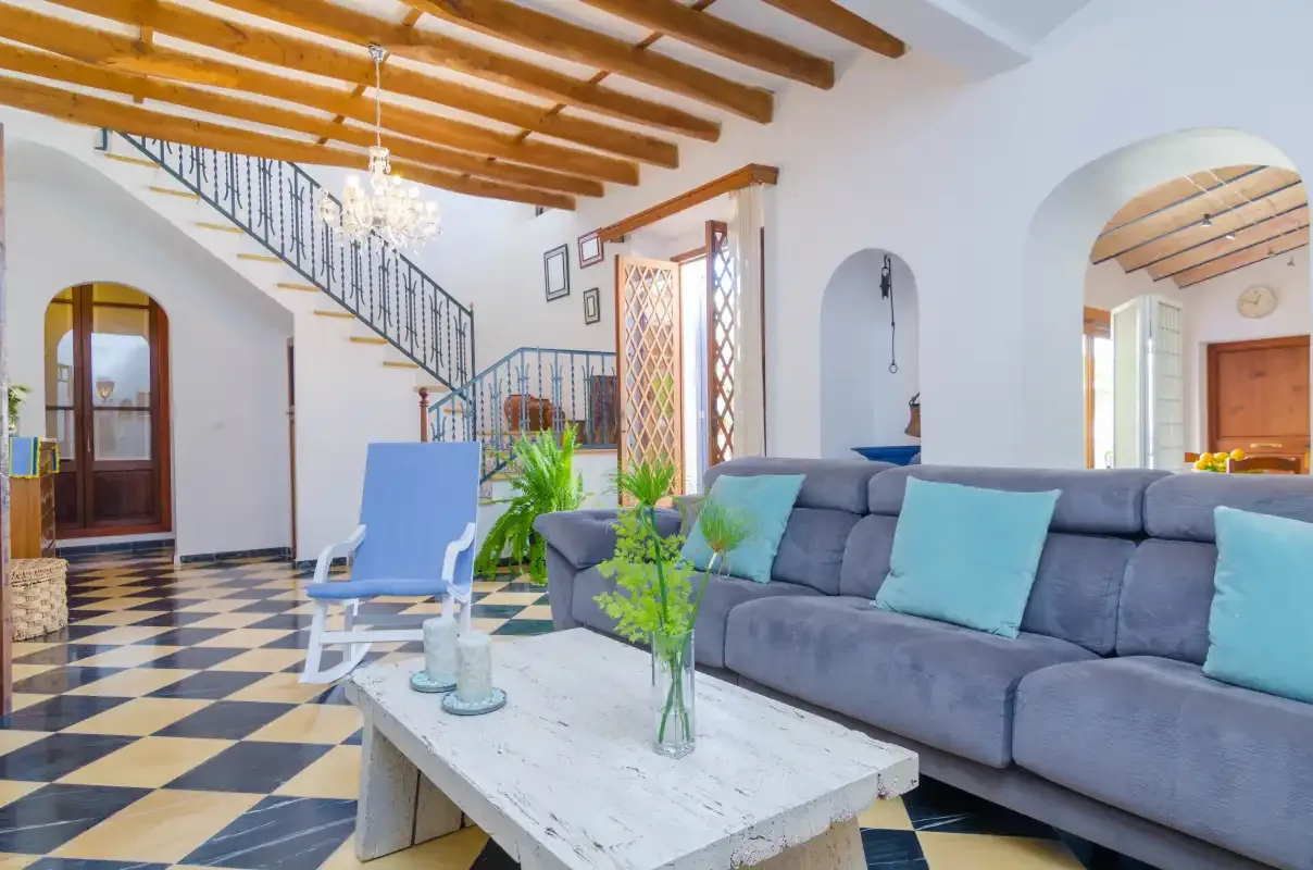 A bright living room with a gray sofa, a coffee table, and exposed ceiling beams.