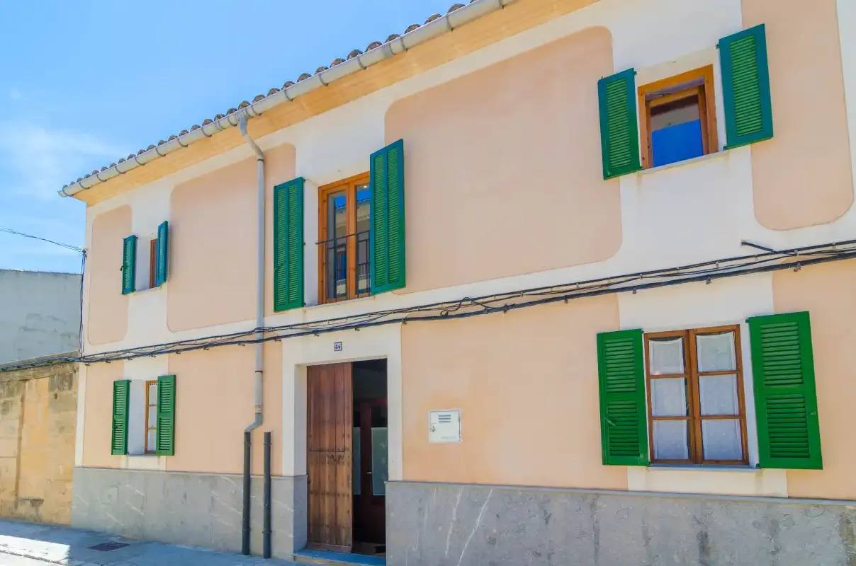 A peach-colored building facade with green shutters and a wooden entrance.