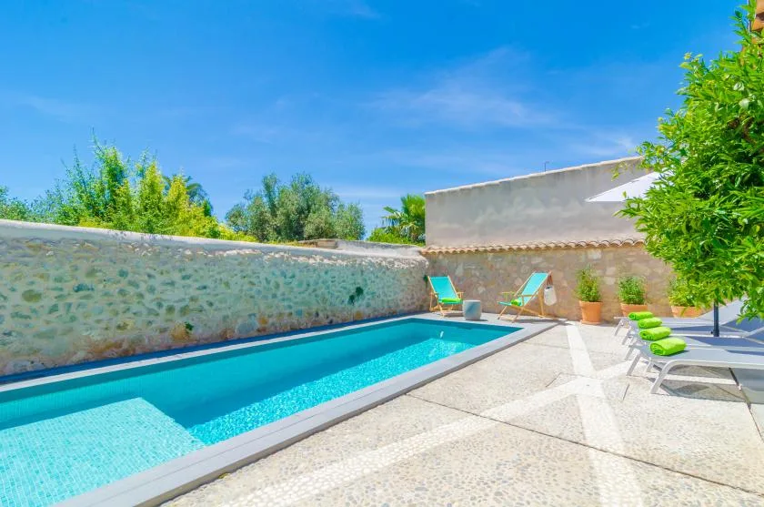 An outdoor swimming pool beside a stone wall and sun loungers.