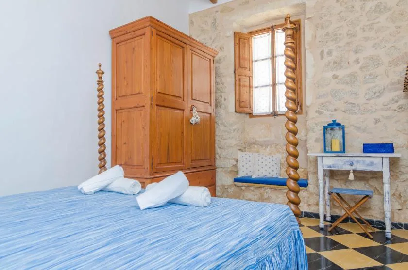 A bedroom with a blue bed, wooden wardrobe, and a window.
