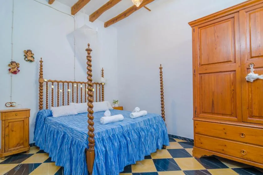 A bedroom with a blue bedspread, wooden furniture, and exposed ceiling beams.