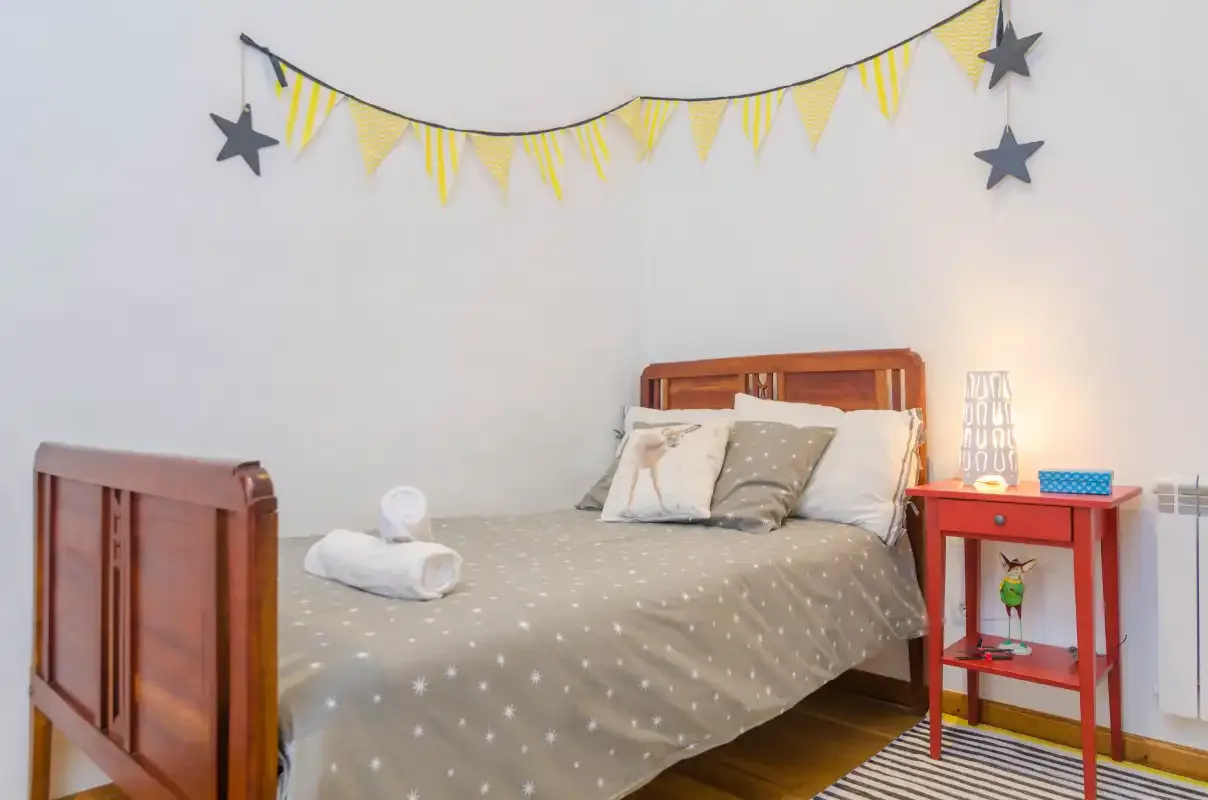 A bedroom with a bed, patterned bedding, and a yellow-and-gray wall garland.