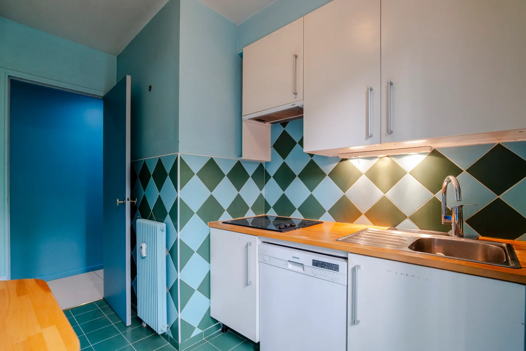 A compact kitchen with white cabinets, a sink, and green patterned tiles.