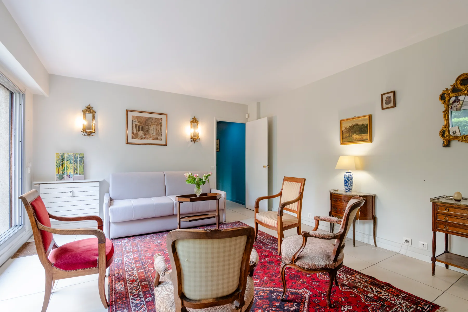 A bright living room with seating arranged around a colorful patterned rug.