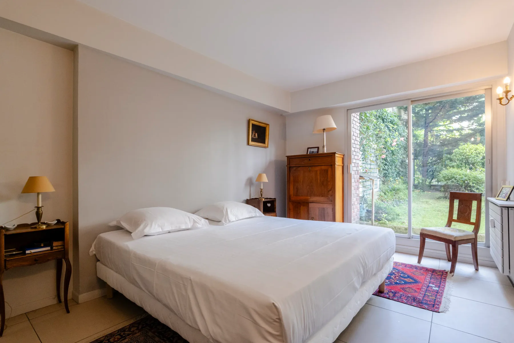 A bedroom with a large bed beside glass doors overlooking greenery.