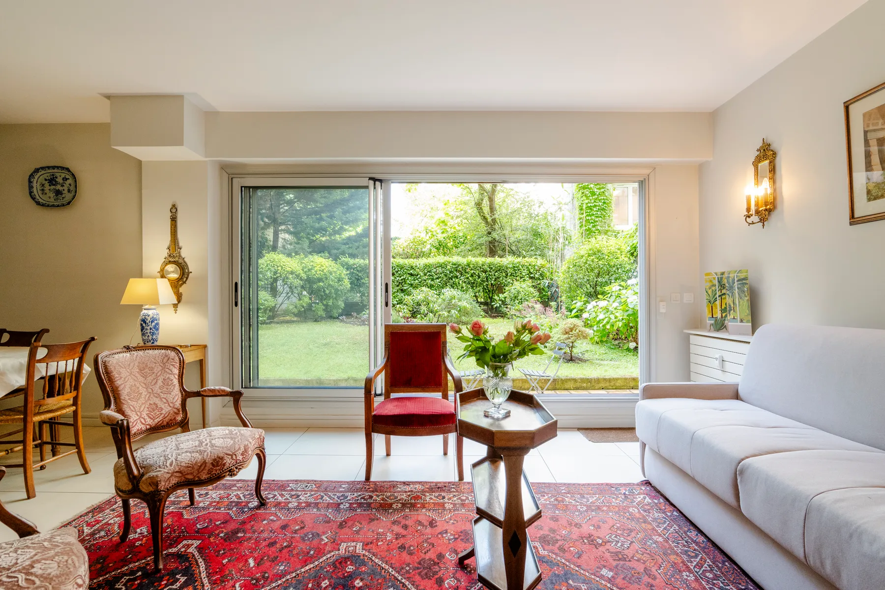 A bright living room with seating beside large windows overlooking a garden.