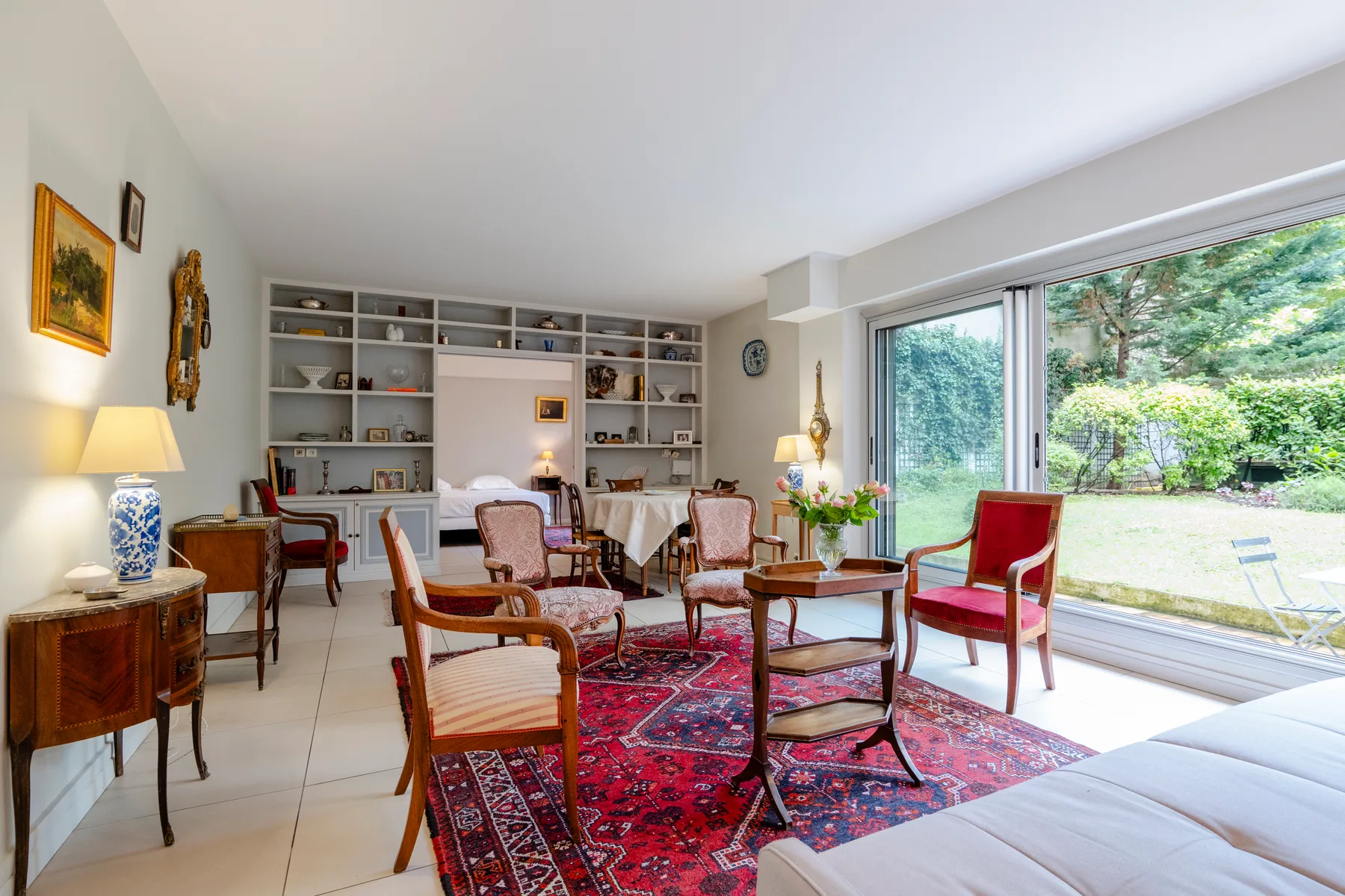 A bright living room has a red patterned rug, seating, and large windows overlooking greenery.