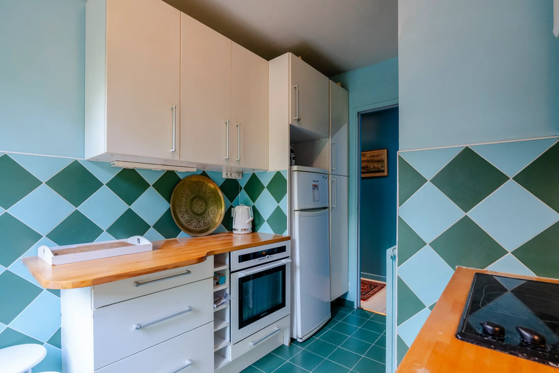 A compact kitchen with white cabinets, green diamond-patterned tiles, and built-in appliances.