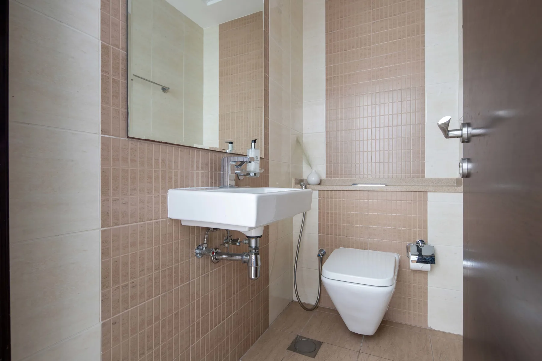 Un baño con lavabo suspendido, inodoro y paredes revestidas de azulejos.