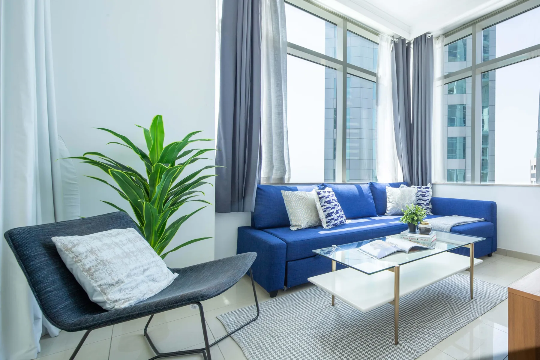 Una sala luminosa con asientos azules junto a grandes ventanas y una mesa de centro de vidrio.