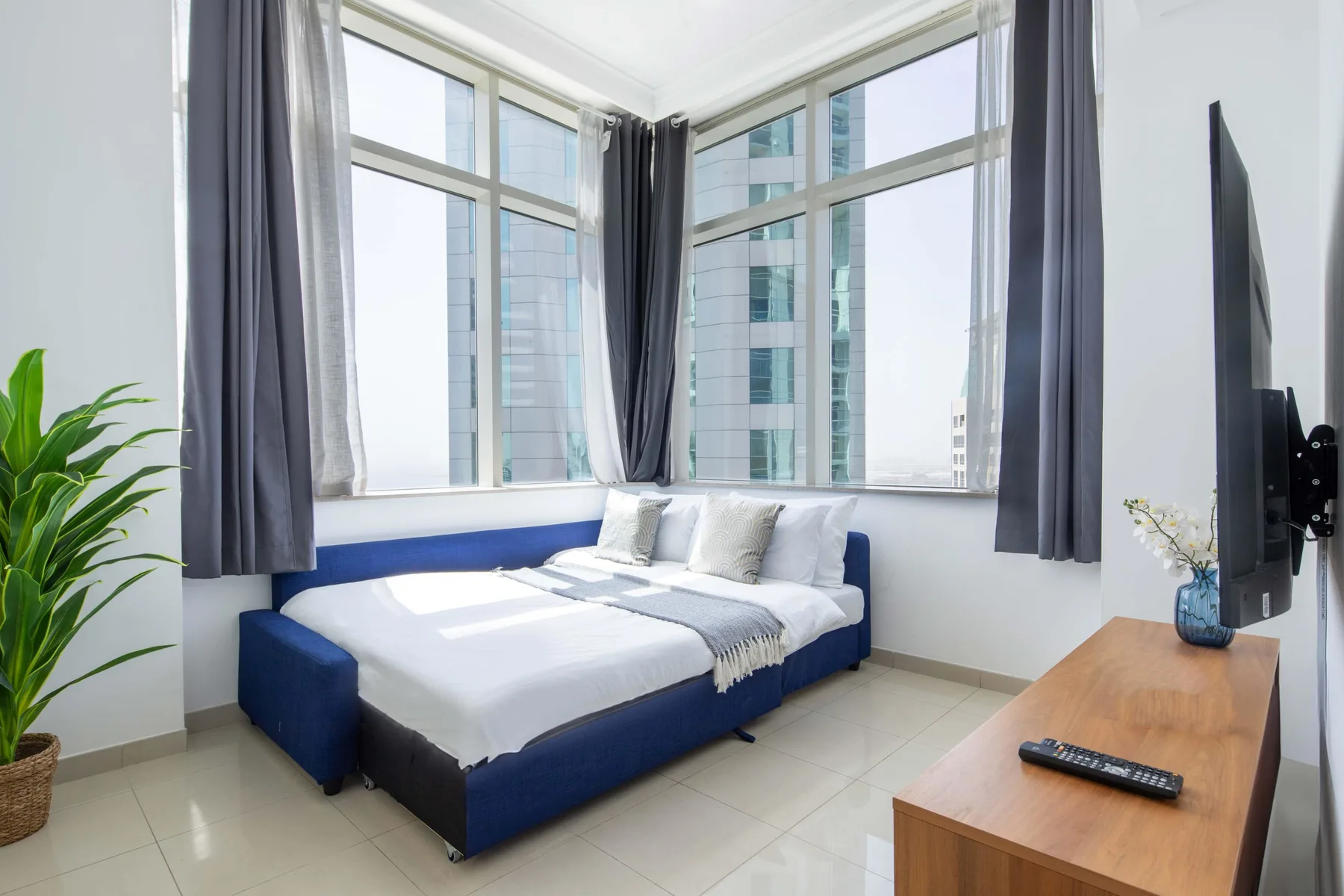 Un dormitorio luminoso con una cama azul junto a grandes ventanas en esquina.