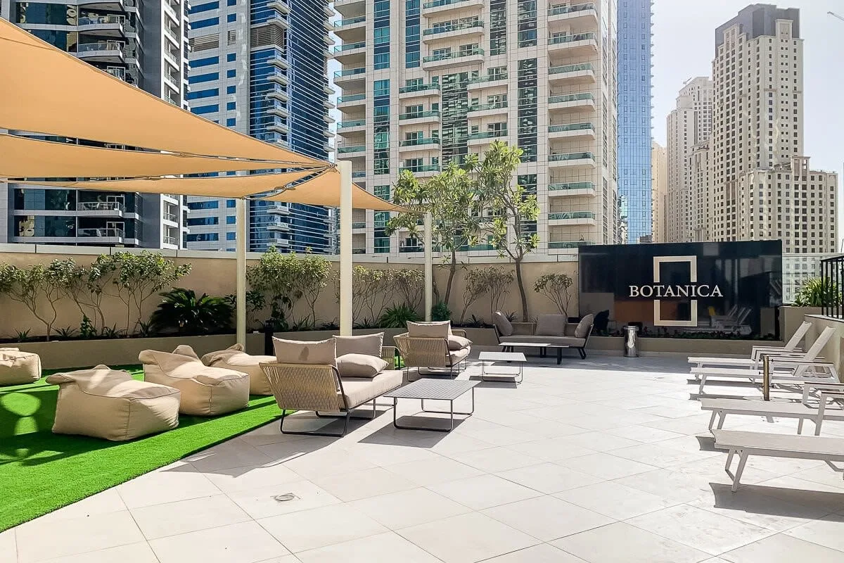 Una terraza exterior tiene asientos, toldos de sombra y césped artificial.
