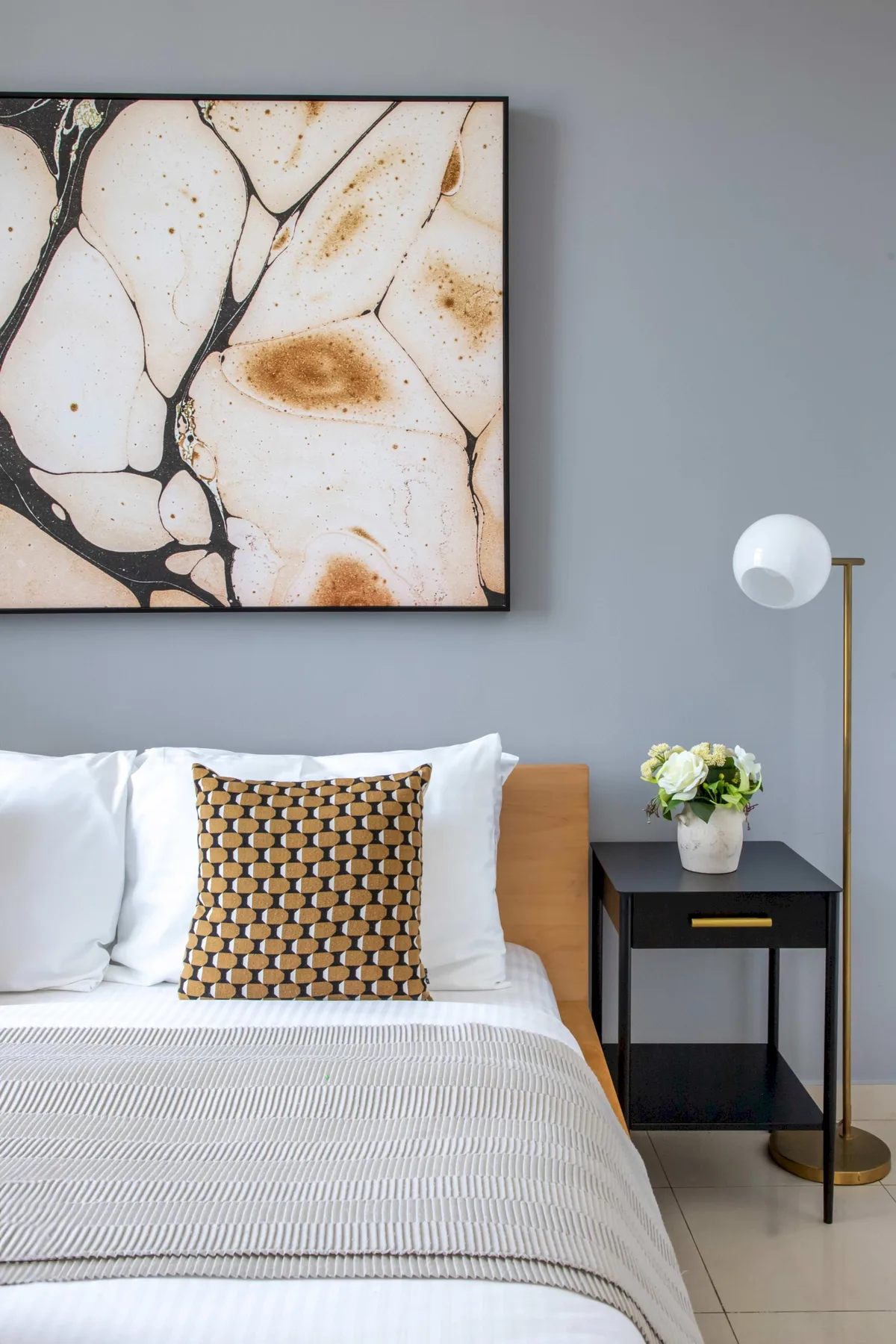 Un dormitorio con una cama bien tendida, un cojín estampado y una obra enmarcada.
