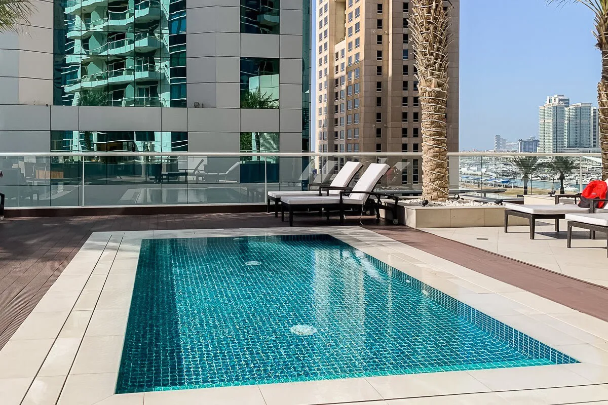 Una piscina en la azotea está junto a una terraza con tumbonas y edificios altos.
