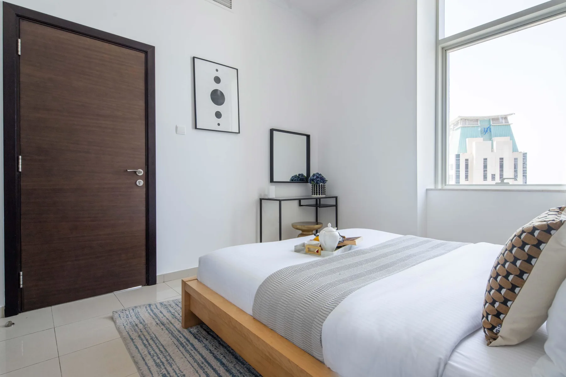Un dormitorio luminoso con una cama de madera, cojines estampados y una ventana grande.