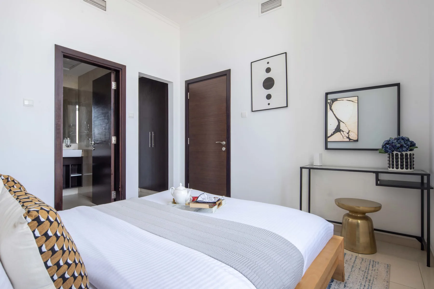 Un dormitorio luminoso con una cama bien tendida y cuadros en la pared.