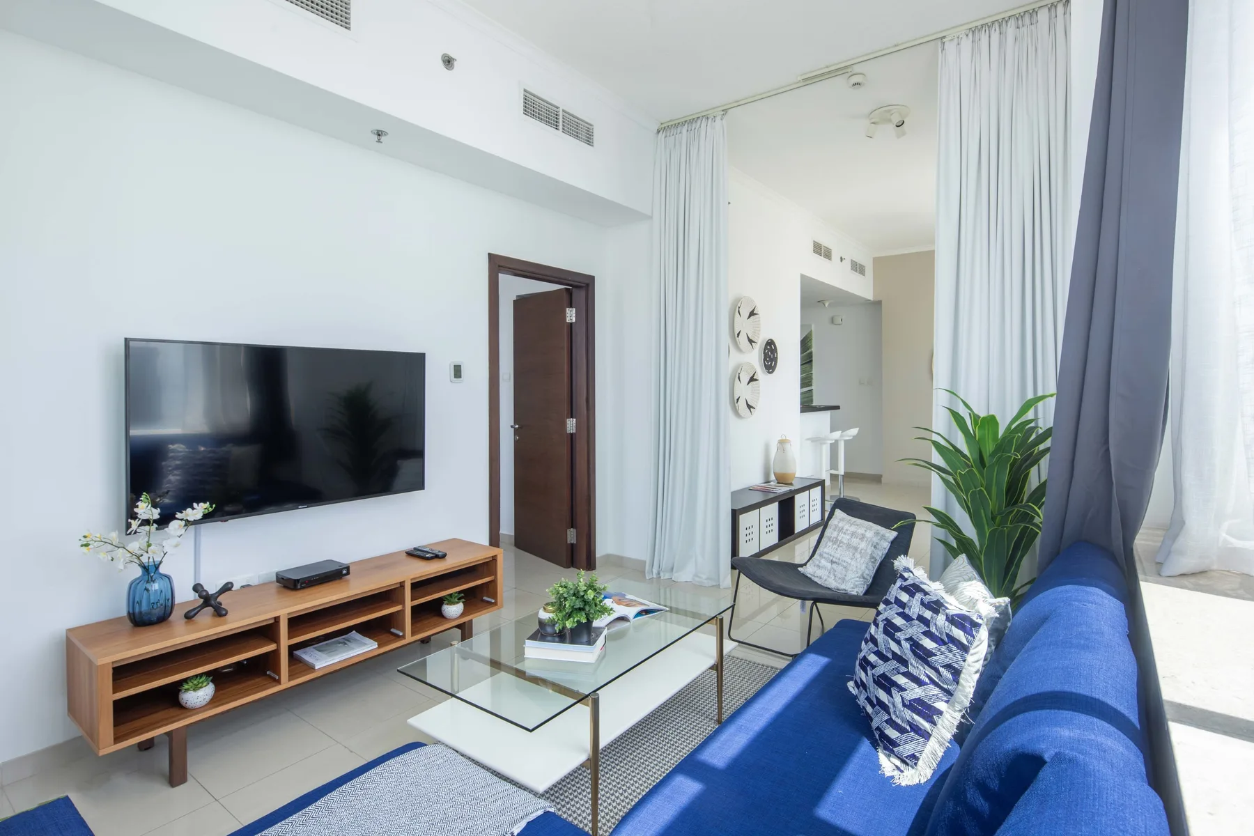 Una sala luminosa con asientos azules, un televisor y una mesa de centro de vidrio.