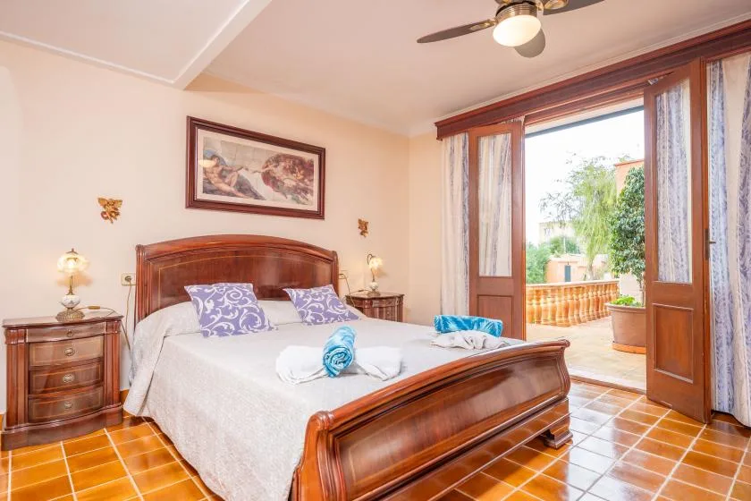 A bedroom with a wooden bed and an open doorway to a sunny terrace.