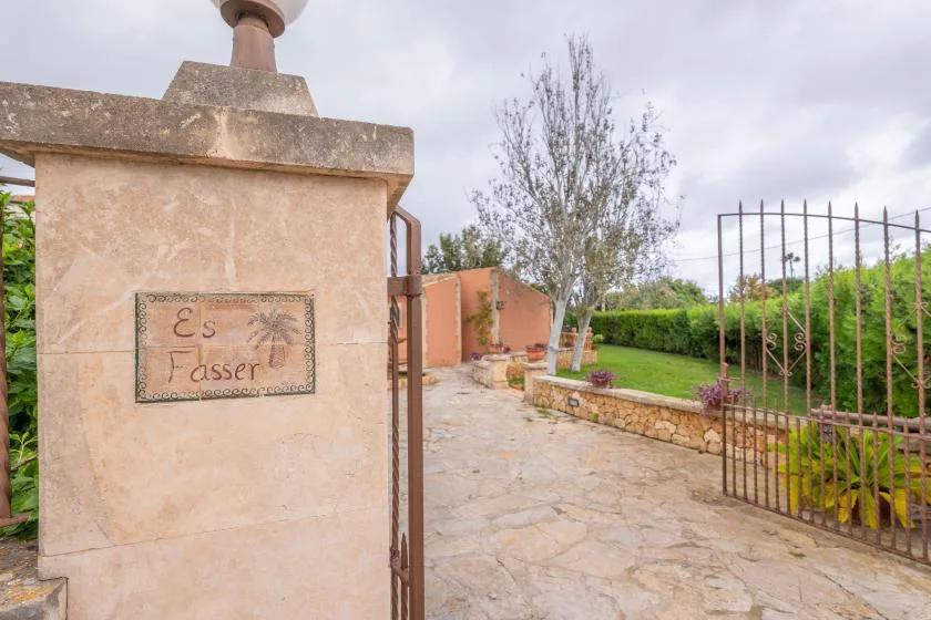 A stone-paved garden entrance with an open metal gate and a tree.