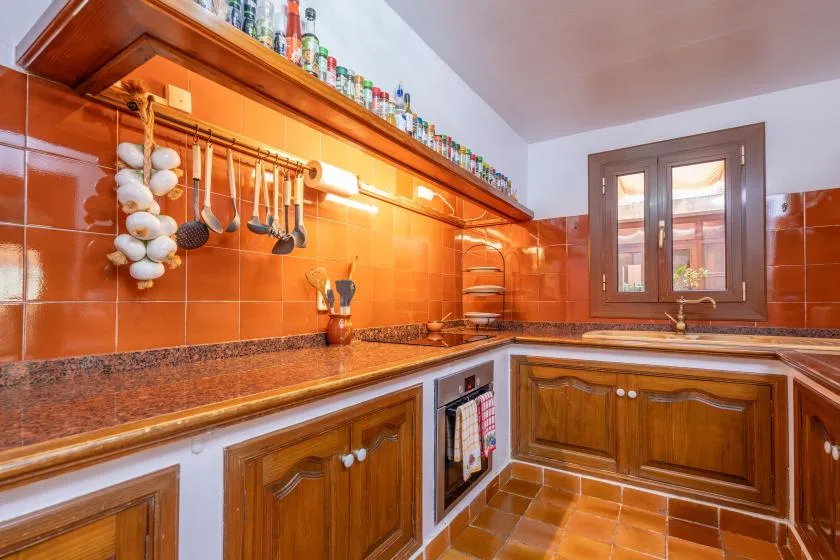 A warm-toned kitchen with wooden cabinets, tiled counters, and a window.