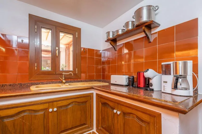 A kitchen with wooden cabinets, orange wall tiles, and a window.