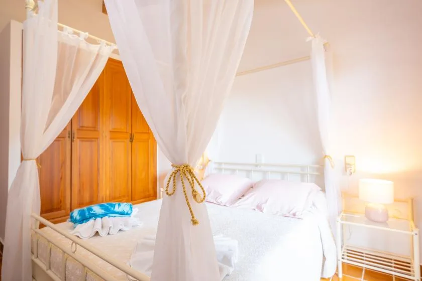 A bedroom with a canopy bed draped in white fabric and a wooden wardrobe.