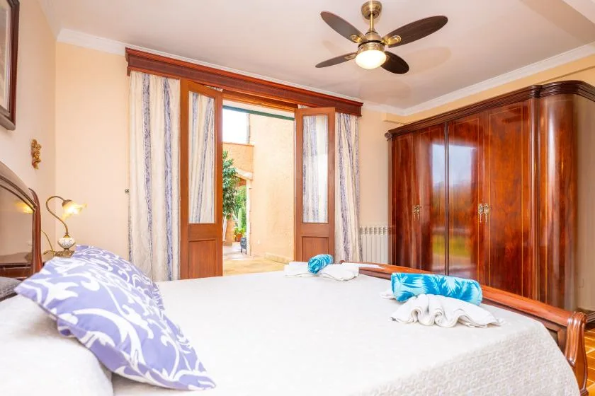 A bedroom with a bed, wooden wardrobe, and open doors to a balcony.