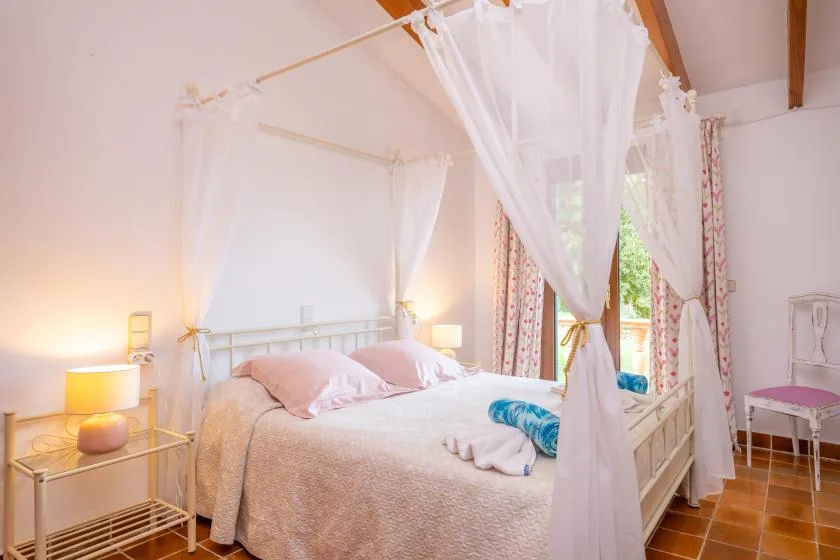 A bedroom with a canopy bed and curtains beside a bright window.