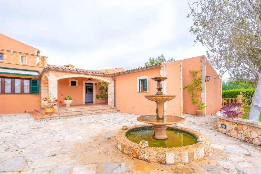 A peach-colored building opens onto a stone courtyard with a fountain.